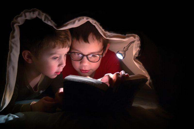 Two children reading a book with a flashlight 